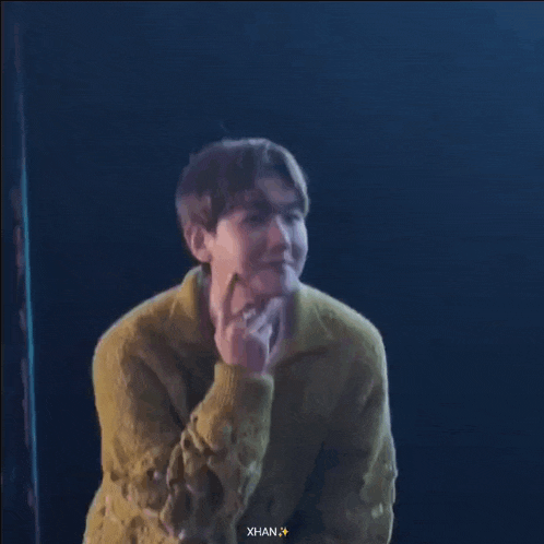 a man in a yellow sweater is making a funny face while sitting on a stage .