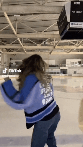 a woman is standing on a ice rink wearing a blue sweater that says ' strong ' on it .