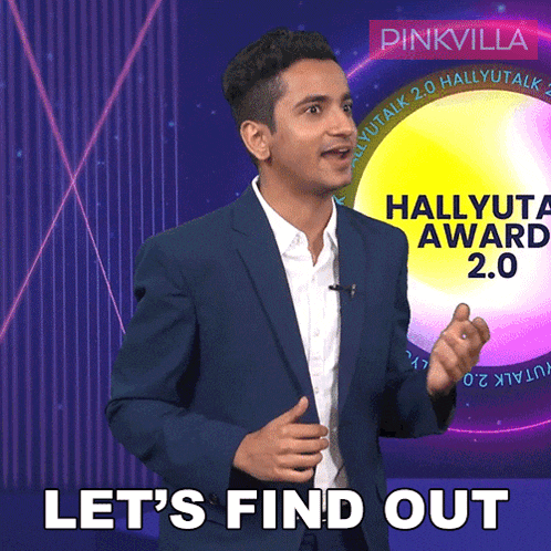 a man in a suit stands in front of a pinkvilla banner