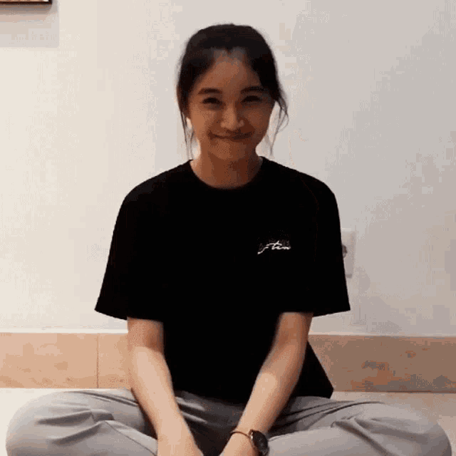 a woman wearing a black t-shirt with the word time on the back sits on the floor with her legs crossed