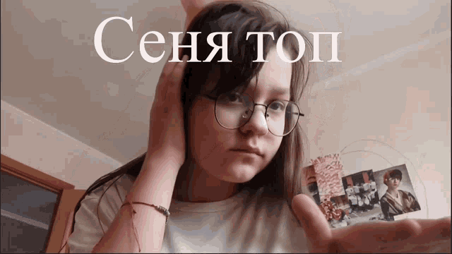a girl wearing glasses and a red bracelet holds her hand up in front of a sign that says ceha top