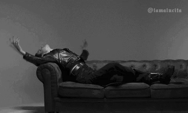 a black and white photo of a woman laying on a couch with her arms outstretched .