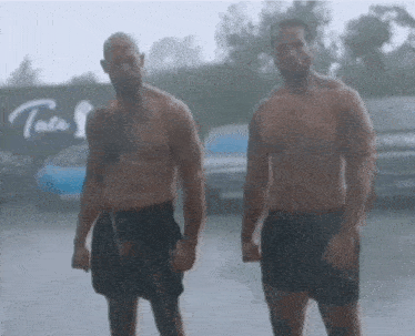 two shirtless men standing next to each other in the rain .