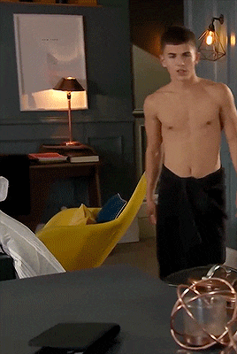 a man without a shirt is standing in a room with a lamp and a picture on the wall that says new york