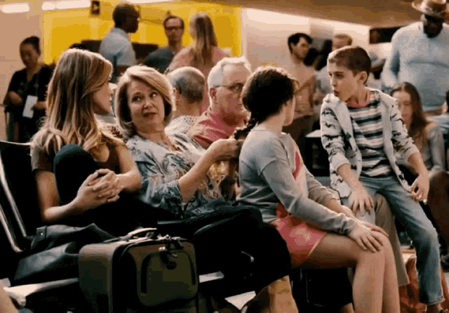 a group of people sitting in a waiting area with a green suitcase in the foreground