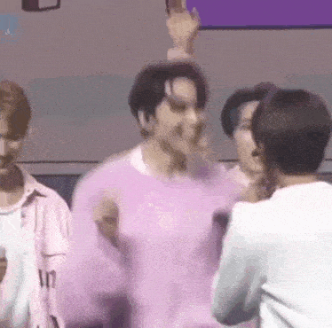 a group of men are standing next to each other in a room . one of the men is wearing a pink sweater .