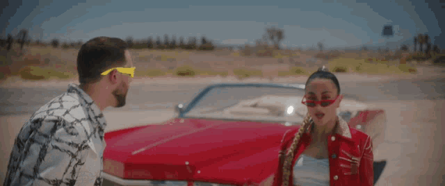 a man and woman standing next to a red car