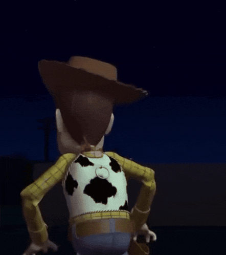 a toy story woody doll is standing in the dark with his arm outstretched .