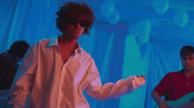 a man wearing sunglasses and a white shirt is dancing in front of a blue background
