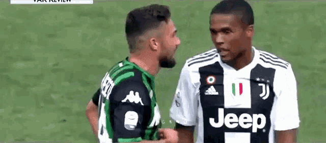two soccer players are standing next to each other on a field and one of them is wearing a jeep shirt .