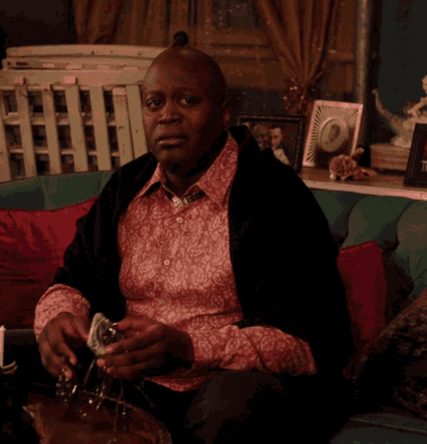 a man in a pink shirt sits on a couch smoking