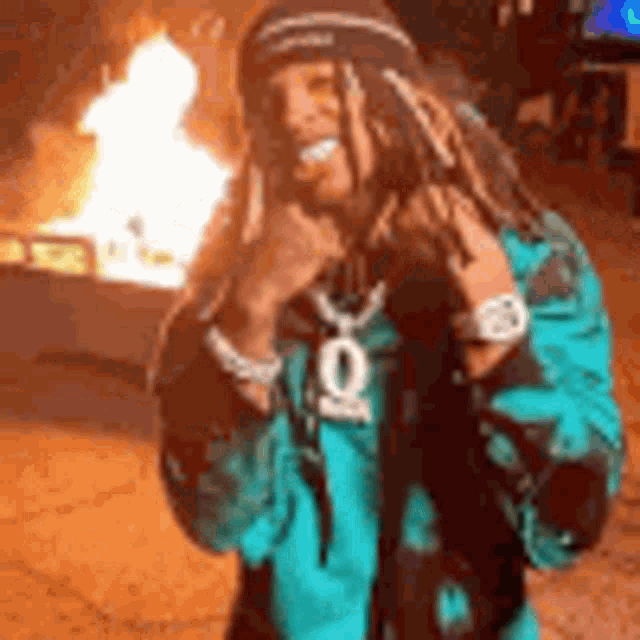 a man wearing dreadlocks and a hat is standing in front of a fire pit .