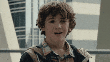 a young boy with curly hair is wearing a plaid shirt and a hooded jacket