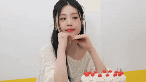 a woman is sitting at a table with a birthday cake with cherries on top .