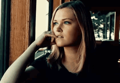a woman is sitting in front of a window with her hand on her chin .