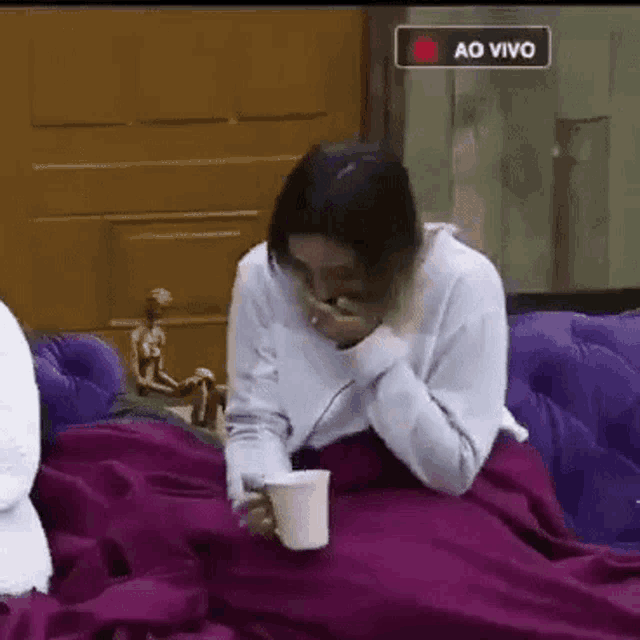 a woman is sitting on a couch with a purple blanket and a cup of coffee .