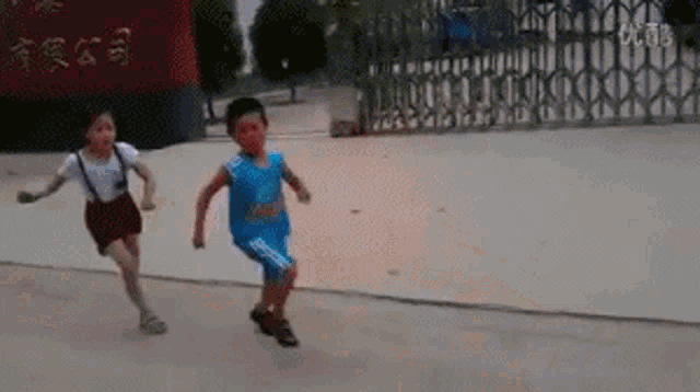 a boy and a girl are running in front of a gate with chinese writing on it .