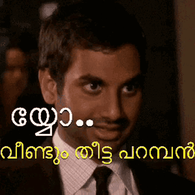a man in a suit and tie is smiling in front of a sign that says ' malayalam '