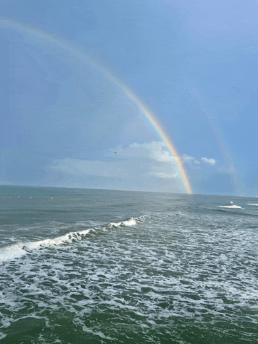 a rainbow appears over the ocean with waves crashing on the shore
