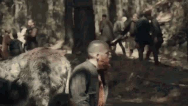 a man with blood on his face is walking through a forest with a group of people behind him .
