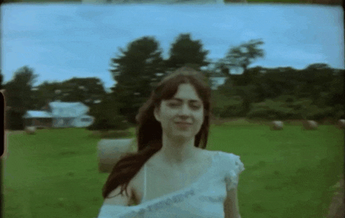 a woman in a white dress is standing in a field with hay bales .