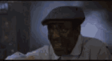 a man wearing a hat and a white shirt is pointing at the camera .