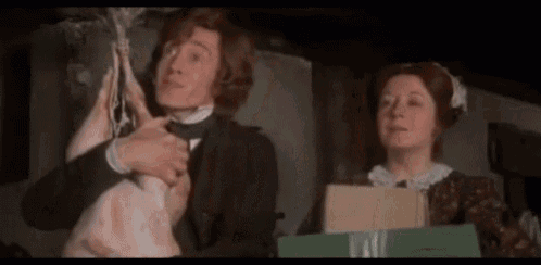 a man and a woman are standing next to each other in a room . the man is holding a piece of meat .