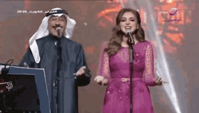 a woman in a pink dress is singing into a microphone next to a man in a keffiyeh .