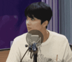 a man is sitting in front of a microphone and looking at the camera .