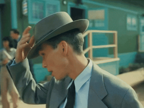 a man in a suit adjusts his hat in front of a barber shop