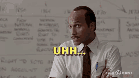 a man in a suit and tie is standing in front of a whiteboard and making a funny face .