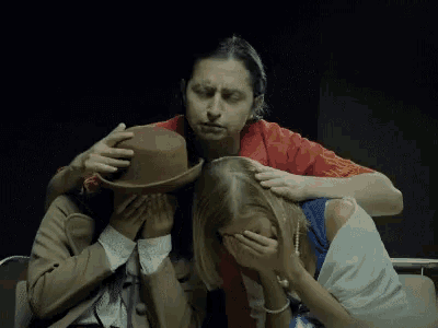 a man in a red shirt is covering a woman 's eyes