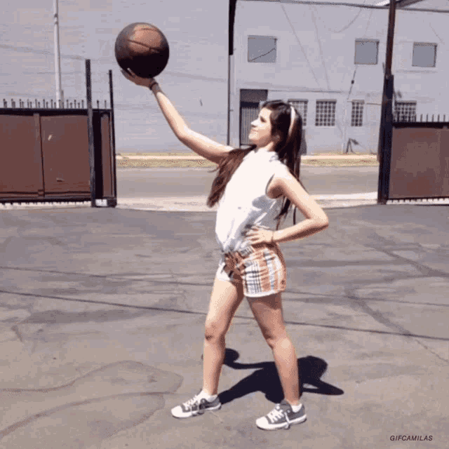 a girl is holding a basketball in her hand and the gif says gif camilas