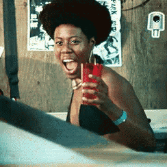 a woman in a bathtub is holding a red drink in her hand and smiling