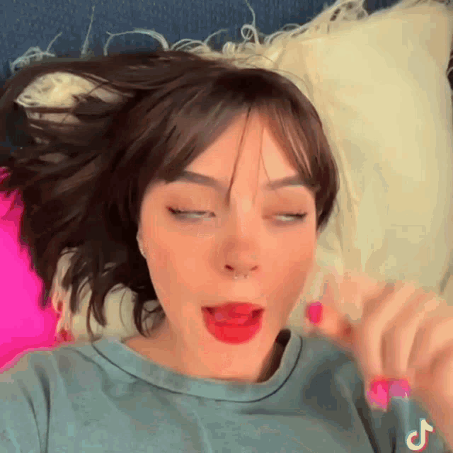 a woman with red lipstick and a nose ring is laying on a bed with a pink pillow