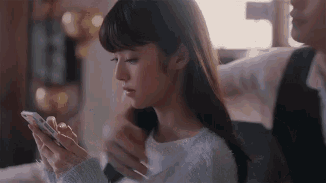 a woman in a white sweater is looking at her phone .