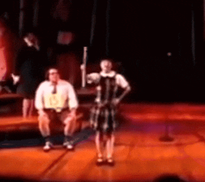 a man sits on a bench while a woman stands on a stage holding a stick