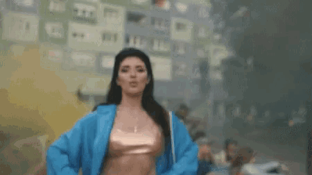 a woman in a blue jacket is dancing in front of a building in a city .