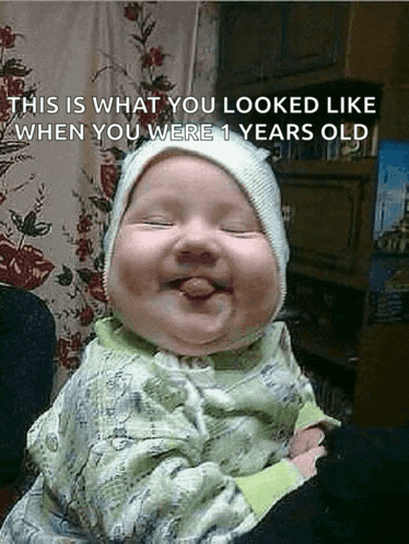 a baby is smiling and sticking out his tongue while wearing a white hat .