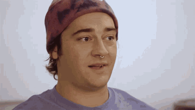 a man wearing a beanie and a nose ring looks at the camera