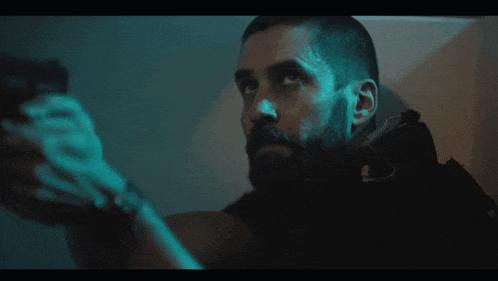 a man with a beard holds a gun in a dark room
