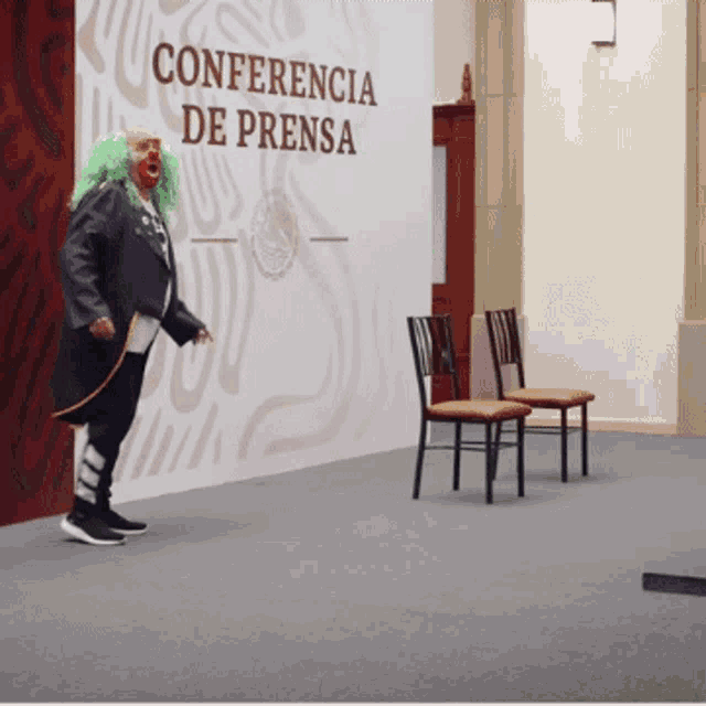 a man in a clown costume stands in front of a wall that says conferencia de prensa