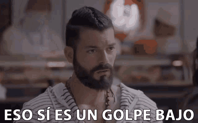 a man with a beard is sitting at a table with the words eso si es un golpe bajo below him