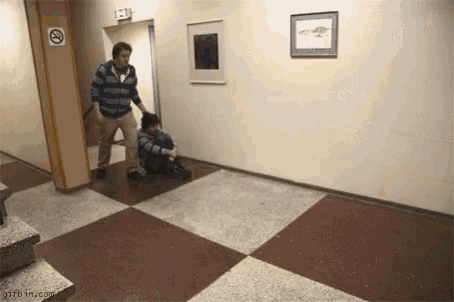a man is standing next to a child sitting on the floor in a hallway .