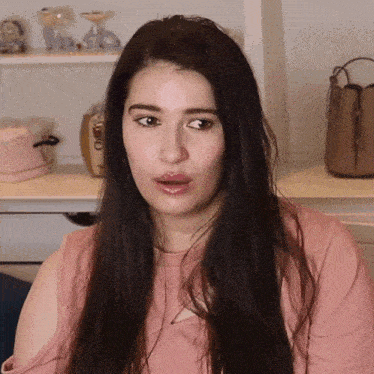 a woman in a pink shirt is sitting in front of a shelf with a purse on it