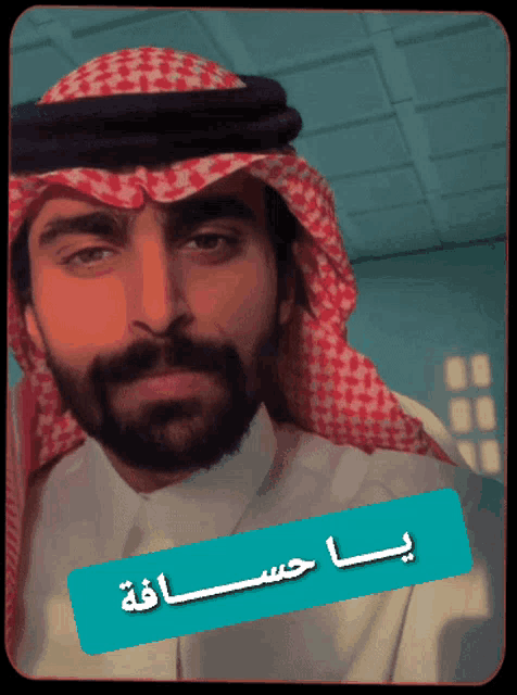 a man with a beard wearing a red and white checkered head scarf with arabic writing on it