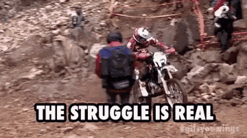 a man is riding a dirt bike on a rocky trail while another man sits on the back of it .