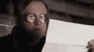 a man wearing glasses is holding a piece of paper and looking at it .