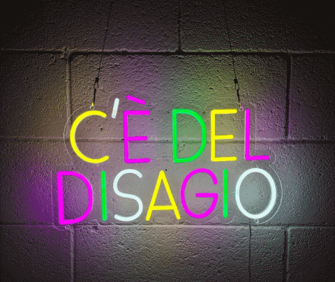 a neon sign that says " ce del disagio " hangs from a brick wall