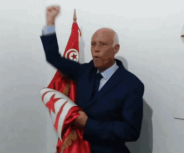 a man in a suit and tie holds up a red flag with a white star on it